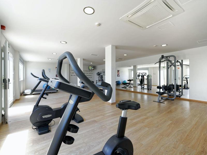 Heller Fitnessraum mit modernen Trainingsgeräten und Holzfußboden.