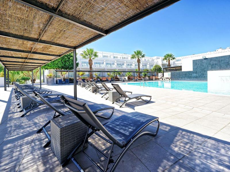 Moderner Poolbereich mit Liegestühlen und schattigem Pergola-Dach am sonnigen Tag.