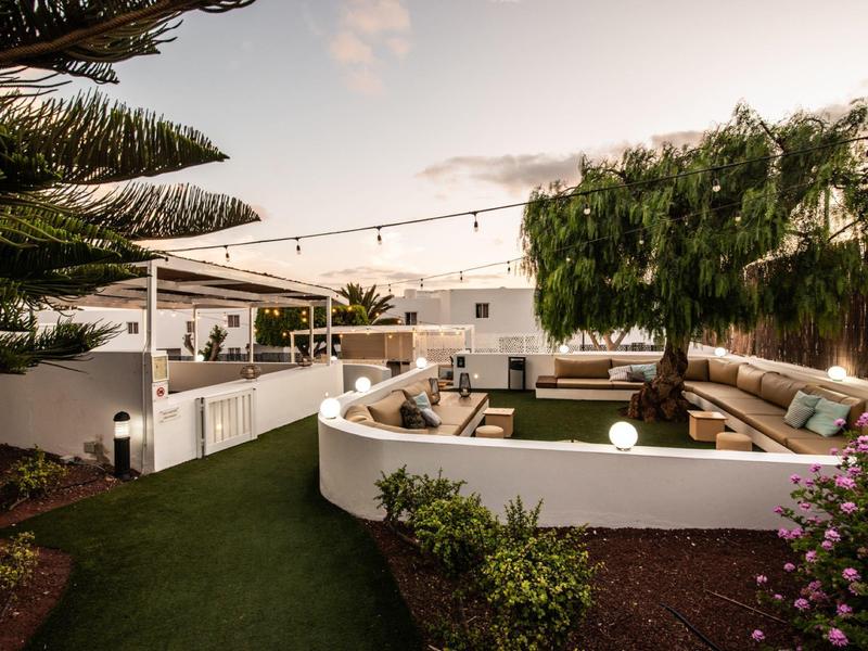 Moderner Garten mit weißen Mauern, grünen Rasenflächen, Sitzbereich und Bäumen im Hintergrund.