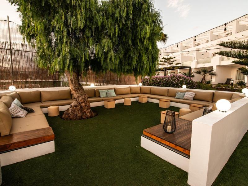 Gemütliche Outdoor-Ecke mit braunen Sitzpolstern, zentralem Baum und grünem Kunstrasen.