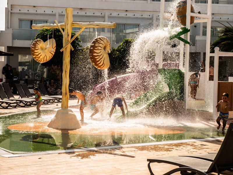 Wasserspielbereich mit Kindern, die unter riesigen Krokodil- und Nautilus-Duschen spielen.