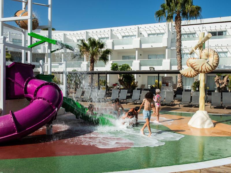 Kinder spielen auf dem spritzenden Wasserspielplatz mit bunten Rutschen unter blauem Himmel.
