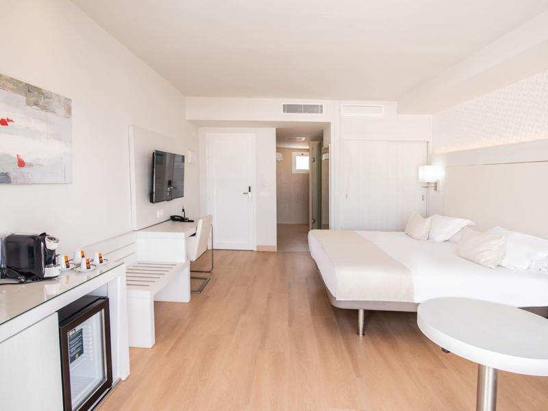 Helles Hotelzimmer mit Doppelbett, Fernseher, Mini-Kühlschrank und Kaffeemaschine, hellem Holzboden.