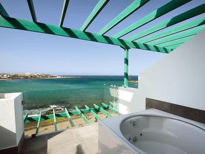Terrasse mit Whirlpool, grüner Pergola und Blick auf das blaue Meer unter klarem Himmel.