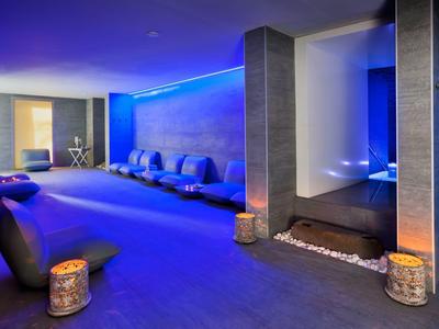 Moderner Spa-Raum mit blauer Beleuchtung, gemütlichen Sitzmöbeln und beruhigenden Dekokaminen.