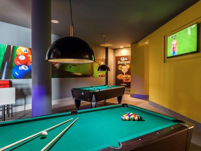 Billardtisch mit Queue, bunte Kugeln, moderne Beleuchtung und Fernseher an gelber Wand in Raum.