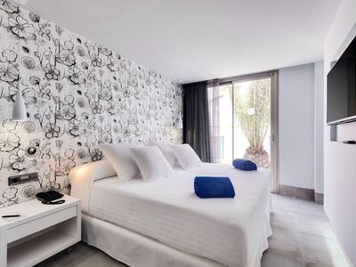 Modernes Hotelzimmer mit zwei weißen Betten, blumiger Wandtapete und großem Fenster mit Balkontür.