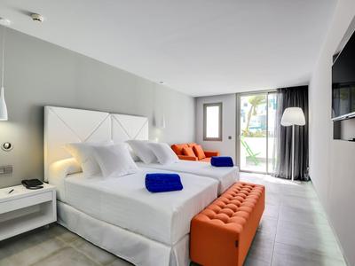 Helles Schlafzimmer mit großem Bett, weißen Wänden, orangen Sitzbank und großer Glas-Schiebetür.