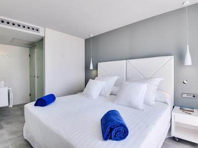 Modernes Schlafzimmer mit weißem Bett, zwei blauen Handtüchern, grauer Wand und minimalistischem Design.