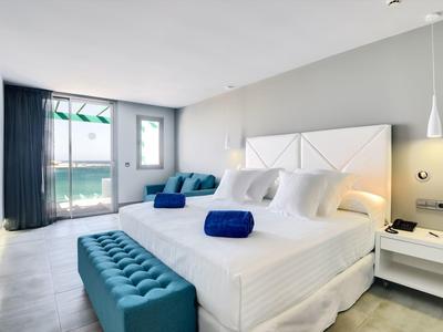 Modernes Schlafzimmer mit großem Bett, blauen Akzenten, Glasfenster und minimalistischer Einrichtung.