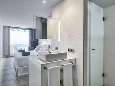 Modernes, helles Hotelzimmer mit Doppelbett, großem Fenster und stilvollem Bad mit Glasdusche.