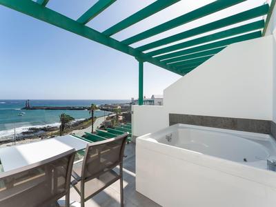 Terrasse mit Whirlpool, Stühlen und Meerblick, weiß-grüne Pergola überdacht, klarer Himmel.