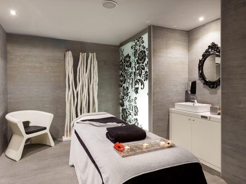 Camera spa elegante con lettino massaggi, sedia bianca e decorazioni moderne.