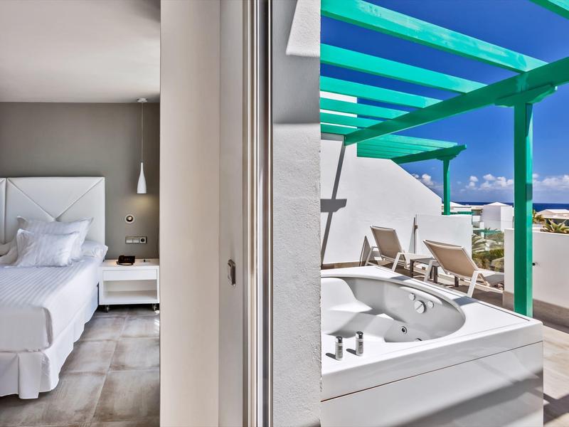 Camera d'hotel bianca e terrazza con vasca idromassaggio esterna e pergolato turchese.