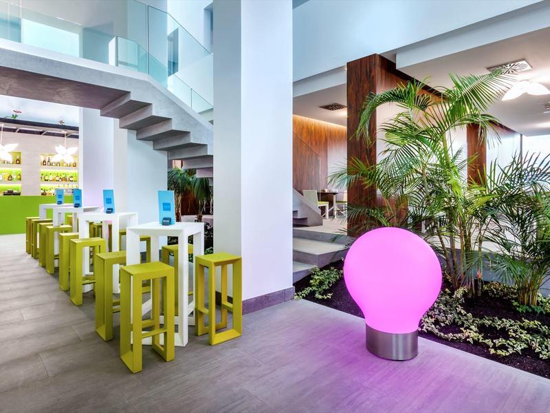 Interno moderno di hotel con scale, piante e luce decorativa rosa.