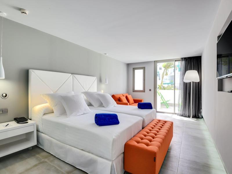 Camera d'hotel moderna con letto matrimoniale, poltrone arancioni e TV a parete.