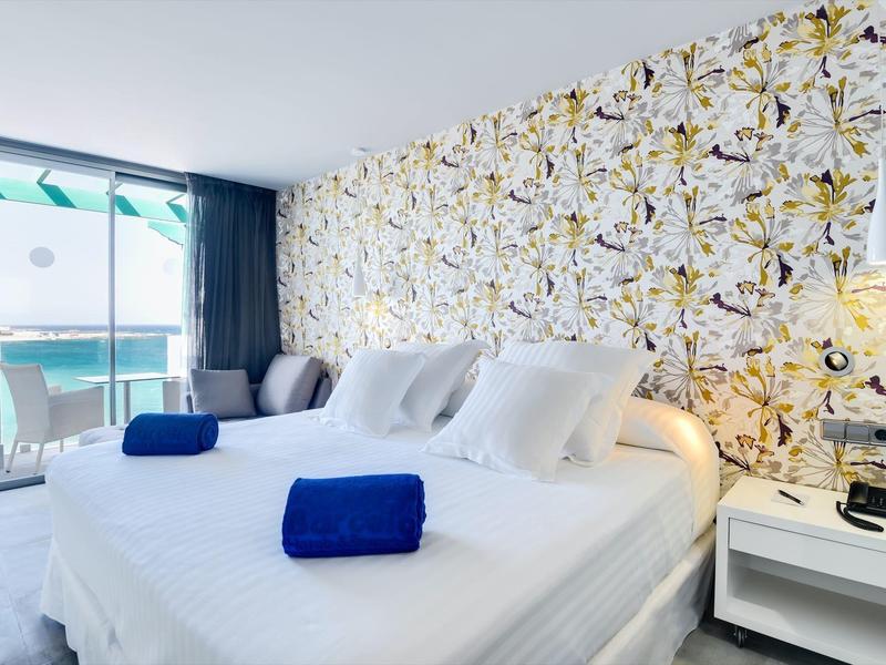 Camera d'hotel moderna con letto grande, pareti fiorite, balcone e asciugamani blu.