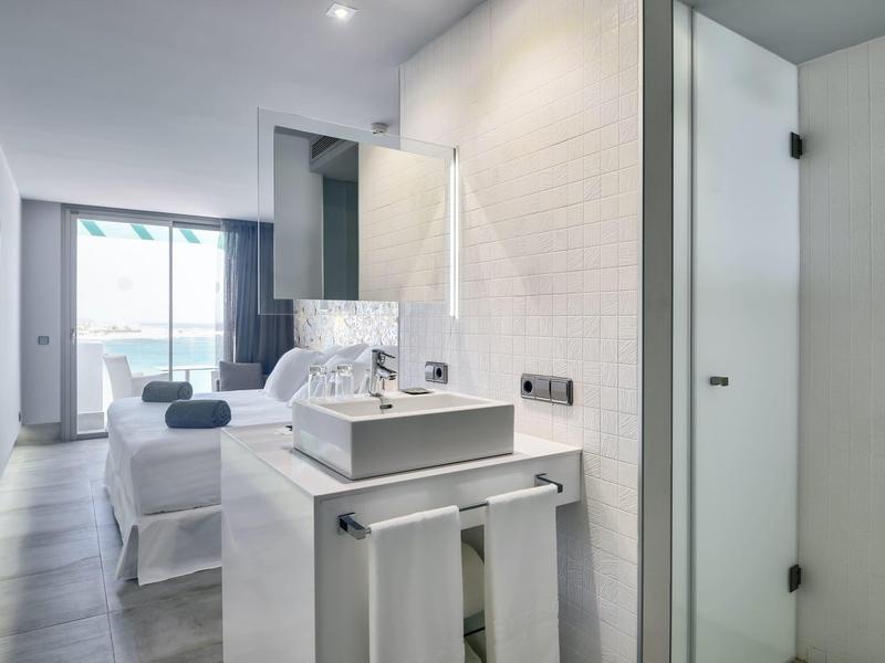 Camera d'hotel moderna con letto, bagno aperto e vista sul mare.