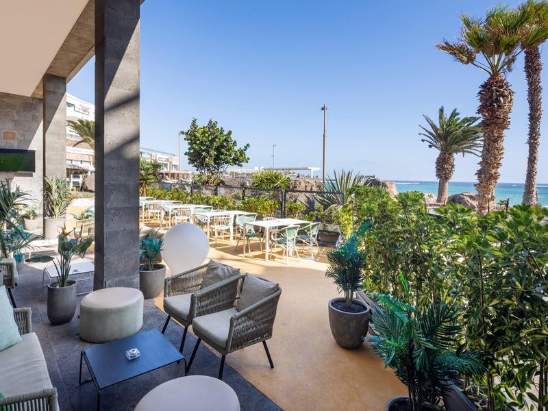 Terrazza dell'hotel con mobili da giardino, vista mare e palme d'estate.