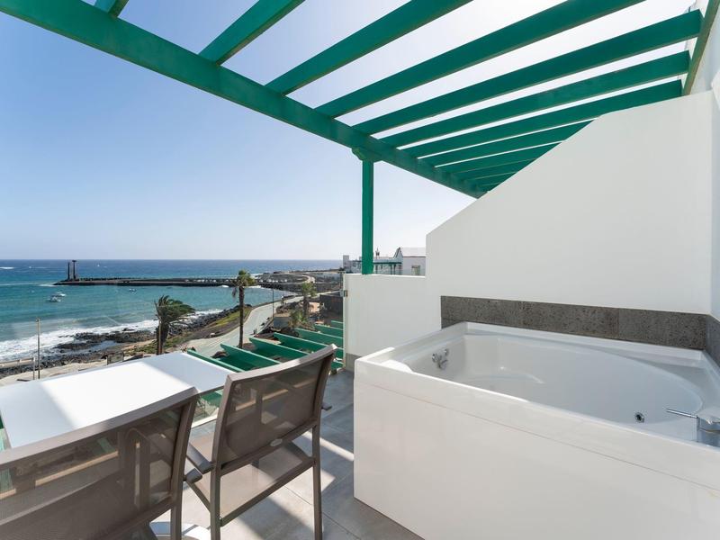 Balcone con vasca idromassaggio e vista mare sotto una pergola verde.