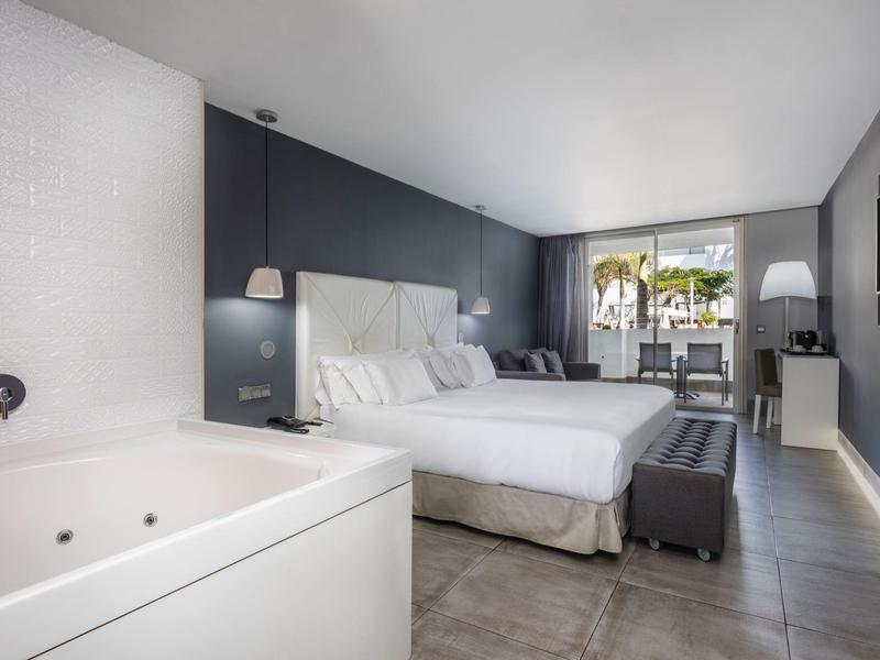 Camera d'hotel moderna con letto matrimoniale, vasca da bagno e balcone con vista sul giardino.