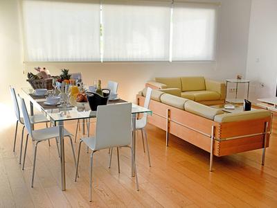 Bright living room with dining area, glass table, white chairs, and yellow sofa by window
