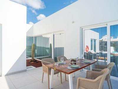 Hell beleuchtete Terrasse mit modernem Esstisch und Stühlen in einem weißen Hotel.