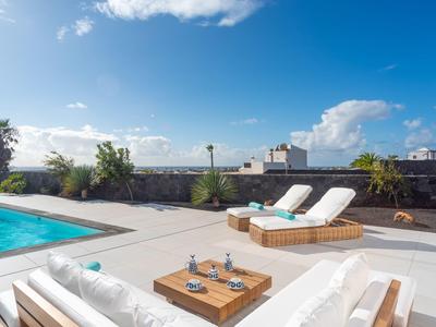 Modern terrace with pool, sun loungers, and blue sky on a sunny day.