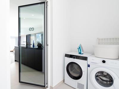 Moderner Waschraum mit weißen Wäschegeräten und Bügeleisen auf einer Ablage.