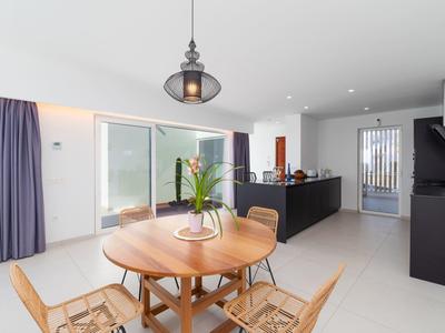 Modern dining area with round wooden table, chairs, and open kitchen in bright room.