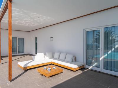 Spacious patio with white corner sofa and wooden table against a white wall and sliding door.