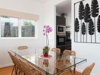Modern dining area with glass table, rattan chairs, and leaf wall art.