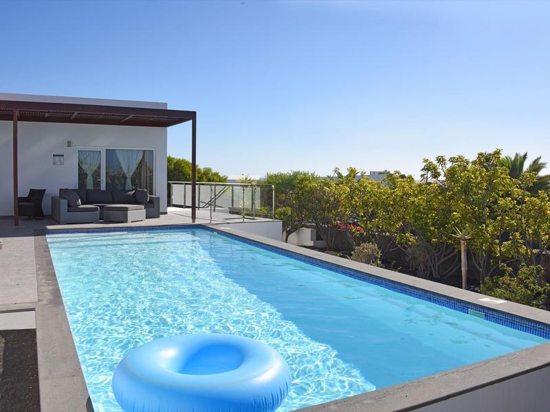 Modern outdoor pool with blue inflatable ring and lounge area under clear sky