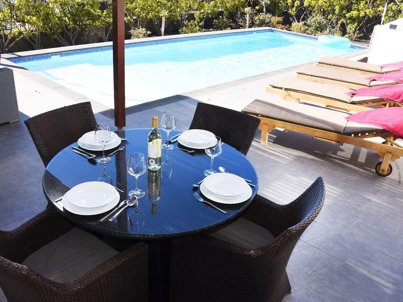 Round dining table set for four next to pool and sun loungers.