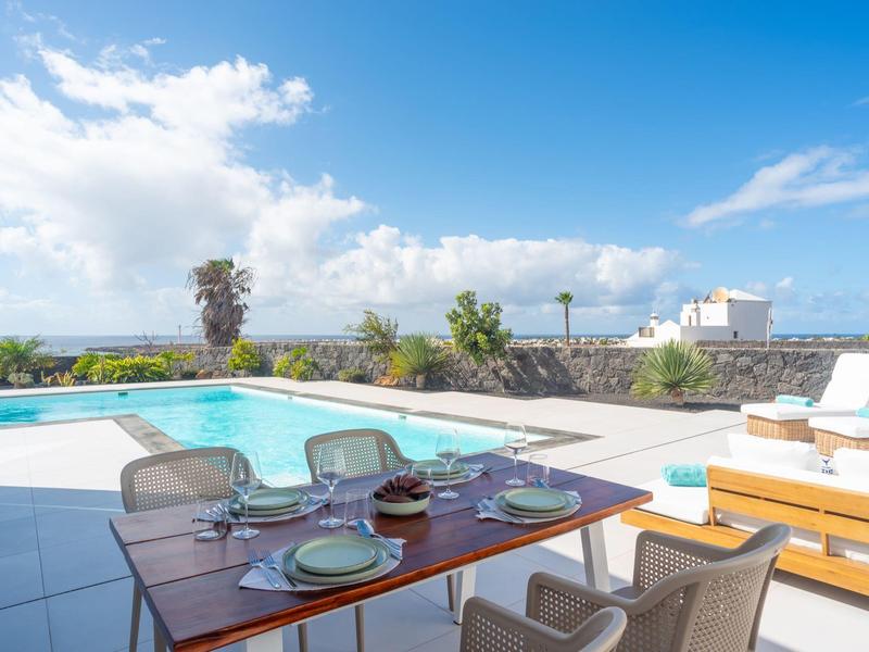 Terrace with table, pool, and sea view under blue sky with some clouds
