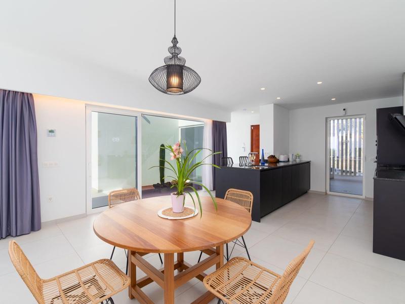 Modern dining area with round wooden table, chairs, and open kitchen in bright room.