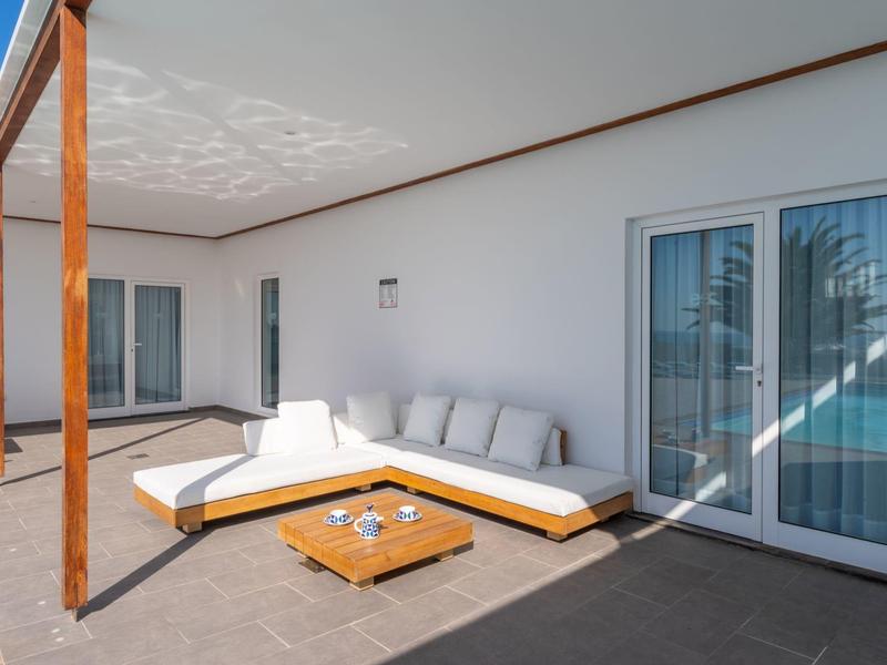 Spacious patio with white corner sofa and wooden table against a white wall and sliding door.
