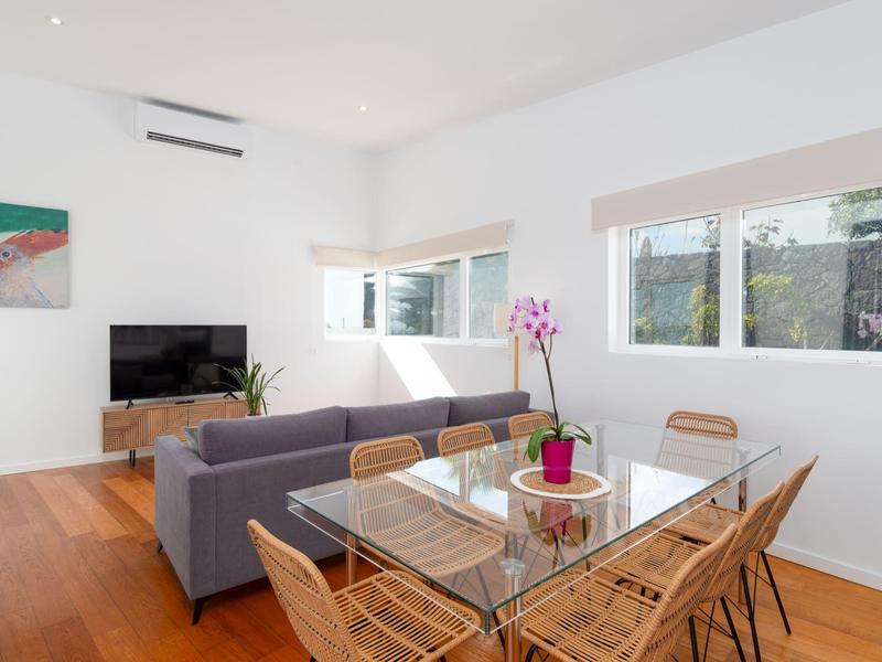 Modern, bright living and dining area with glass dining table and gray sofa.