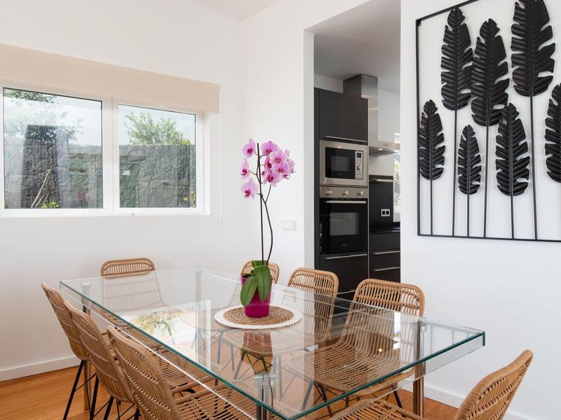 Modern dining area with glass table, rattan chairs, and leaf wall art.
