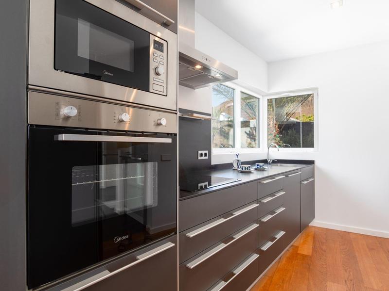 Modern kitchen with built-in stainless steel appliances, black countertops, and wooden floor.