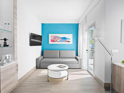 Moderner Wohnraum mit grauem Sofa vor blauem Wandakzent, rundem weißen Tisch und hellem Holzboden.