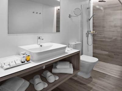 Modernes Badezimmer mit Waschtisch, Spiegel, Dusche, WC und Stauraum für Handtücher und Hausschuhe.