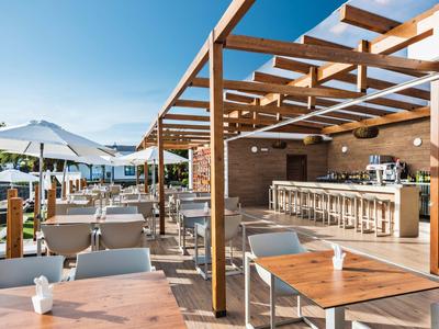 Moderner Außenbereich mit Holzmöbeln, Sonnenschirmen und Holzpergola unter klarem Himmel.