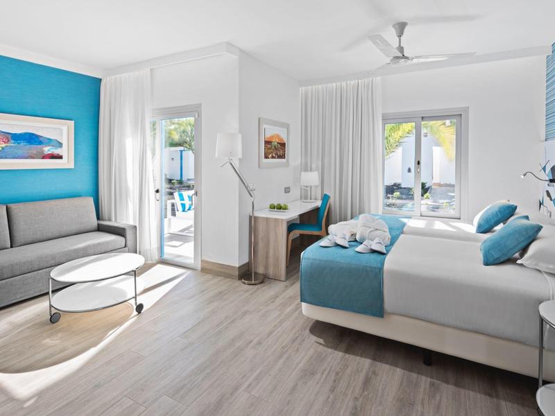 Habitación de hotel moderna con cama doble, escritorio y suelos de madera clara, luminosa y acogedora.