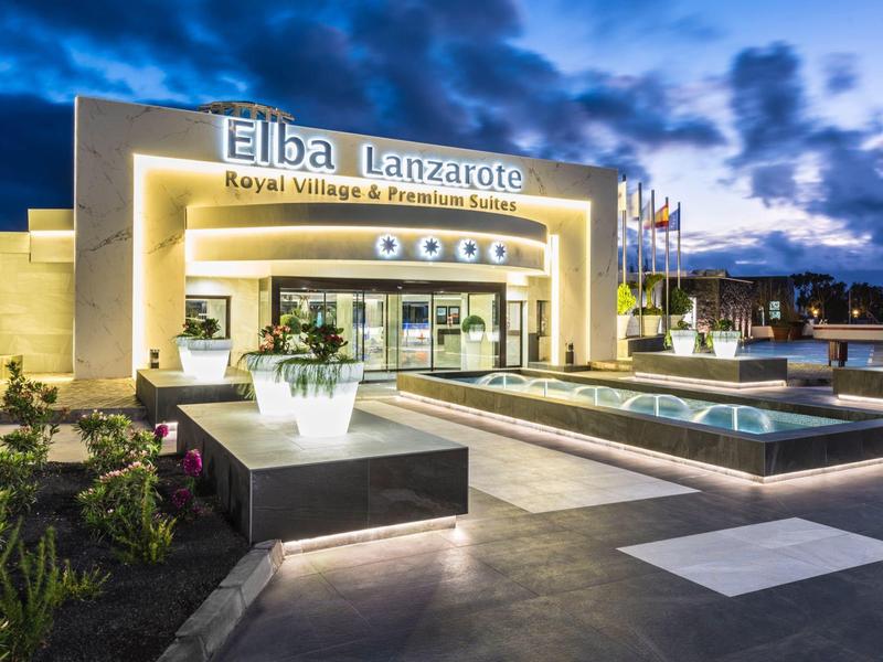 Edificio moderno de hotel con entrada iluminada y fuente al anochecer.