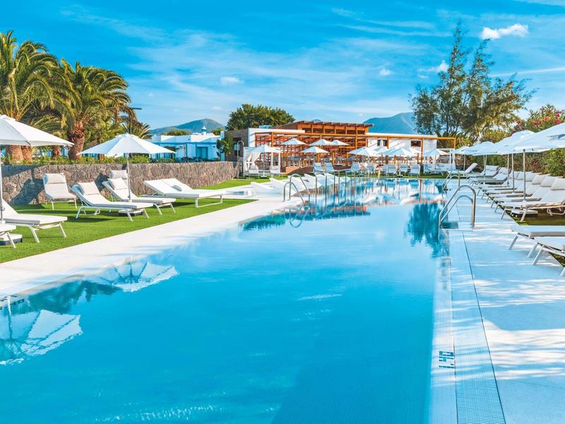 Gran piscina exterior con tumbonas y sombrillas en un complejo hotelero tropical bajo el sol.