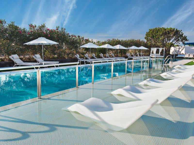 Piscina exterior moderna con tumbonas blancas y sombrillas bajo el cielo azul.
