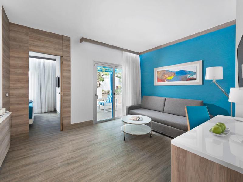 Habitación de hotel moderna con sofá, mesa de centro y acceso a balcón con acento azul en la pared.