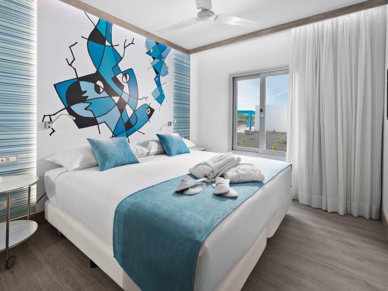 Habitación de hotel moderna con cama doble, acentos azules y pintura abstracta junto a ventana con vistas.