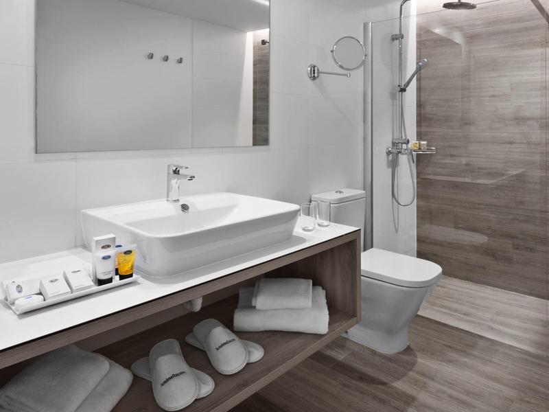 Baño moderno con lavabo, ducha, inodoro y toallas debajo del estante.